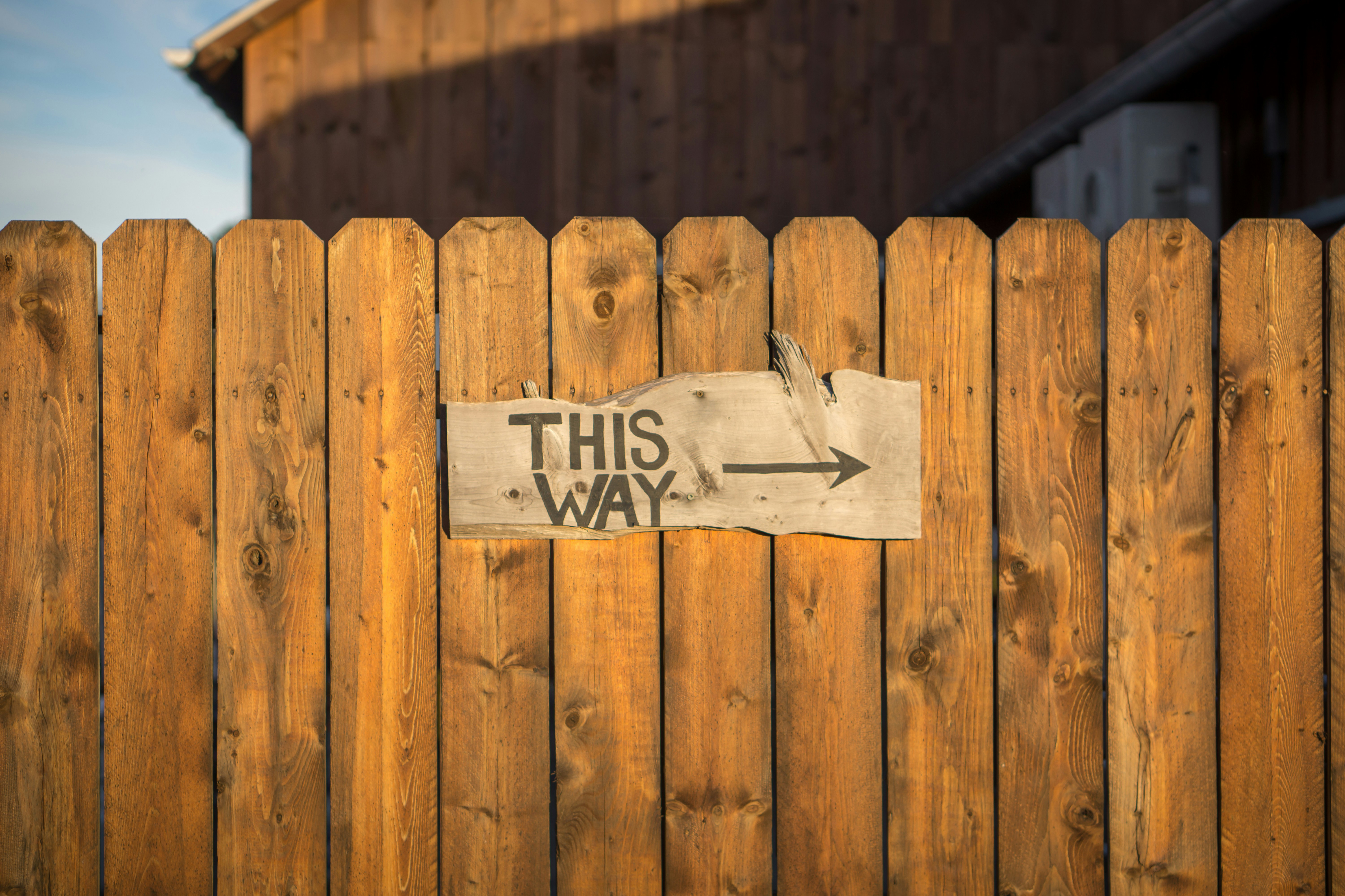 Sign on a wooden fence with handpainted message "This Way" with an arrow pointing to the right